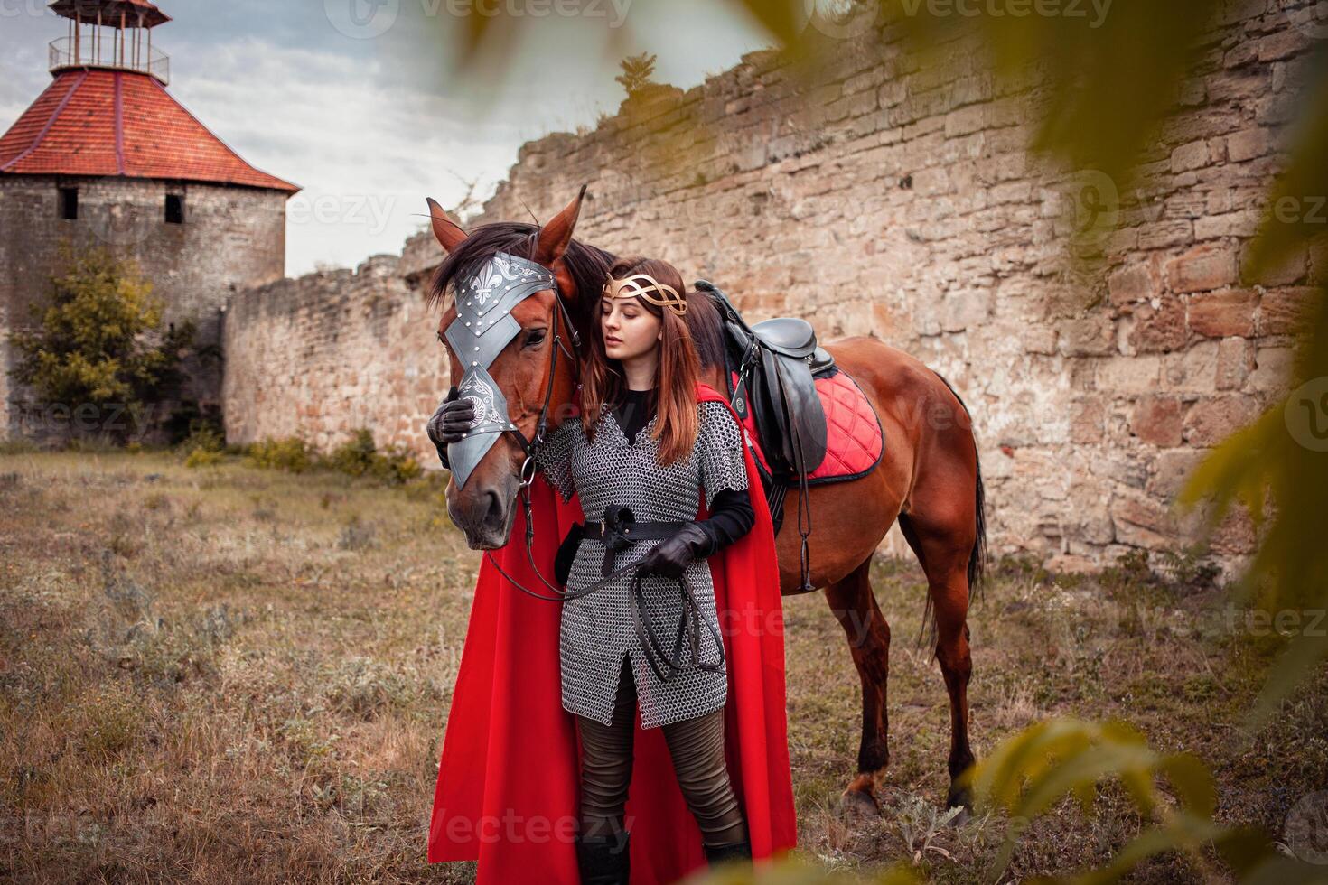 lindo Princesa com vermelho capa carrinhos Próximo para a cavalo contra a pano de fundo do uma torre e uma pedra parede foto