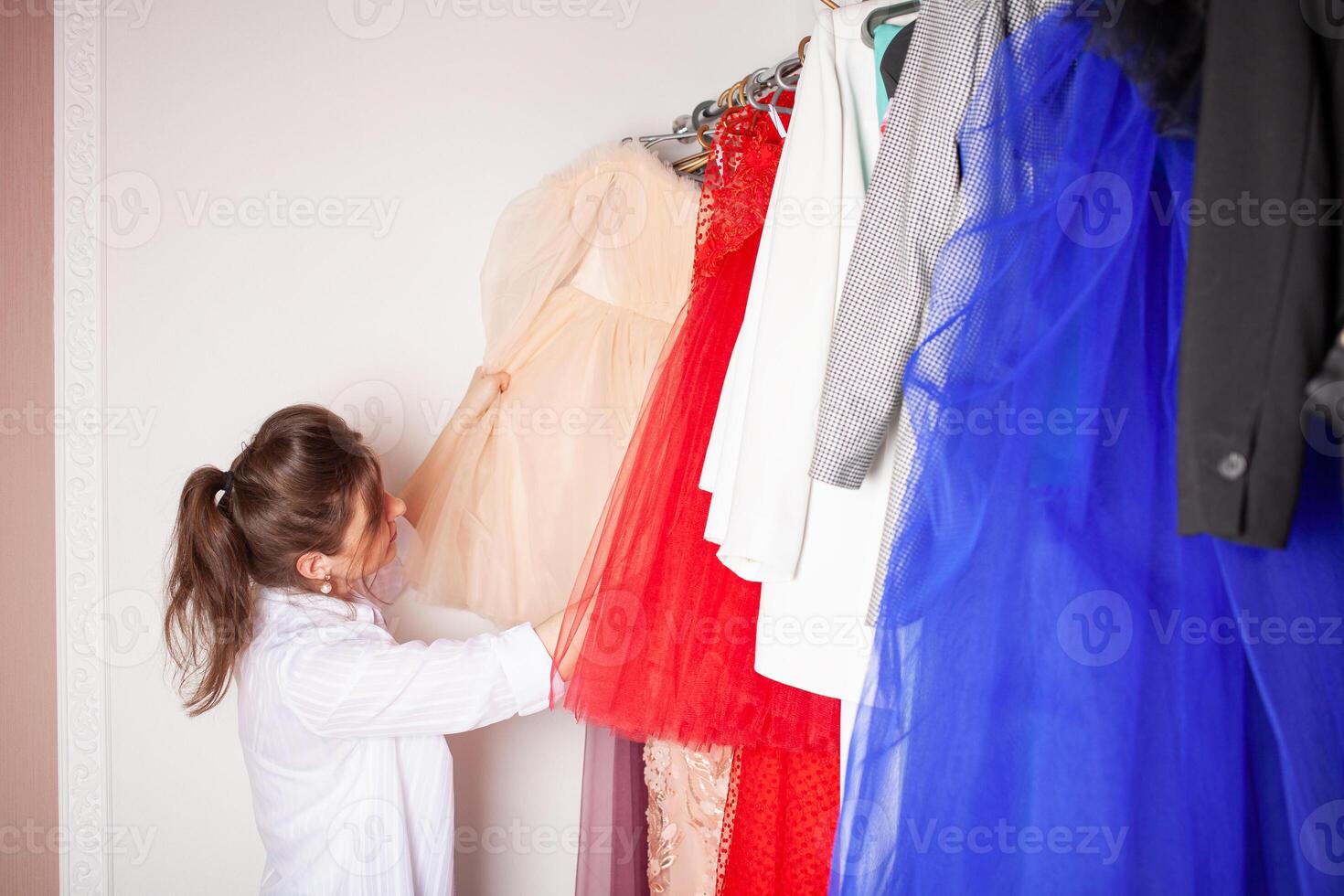 costureira às trabalhar. costureira fazer roupas dentro moderno estúdio. alfaiate segurando lápis e marcação tecido. mulher em pé às mesa com cortar têxtil, de costura máquina, fio, alfinetes, agulhas, fita, recortes foto