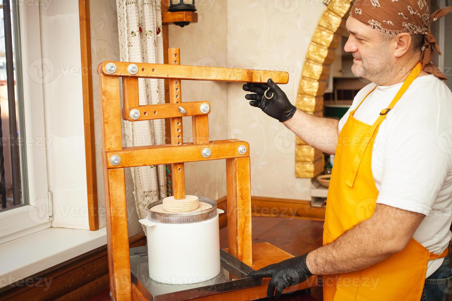 Fabricante de queijos coloca queijo debaixo imprensa, soro de leite. casa Produção, negócios, retrato. de madeira equipamento. uma homem dentro uniforme cozinhando foto