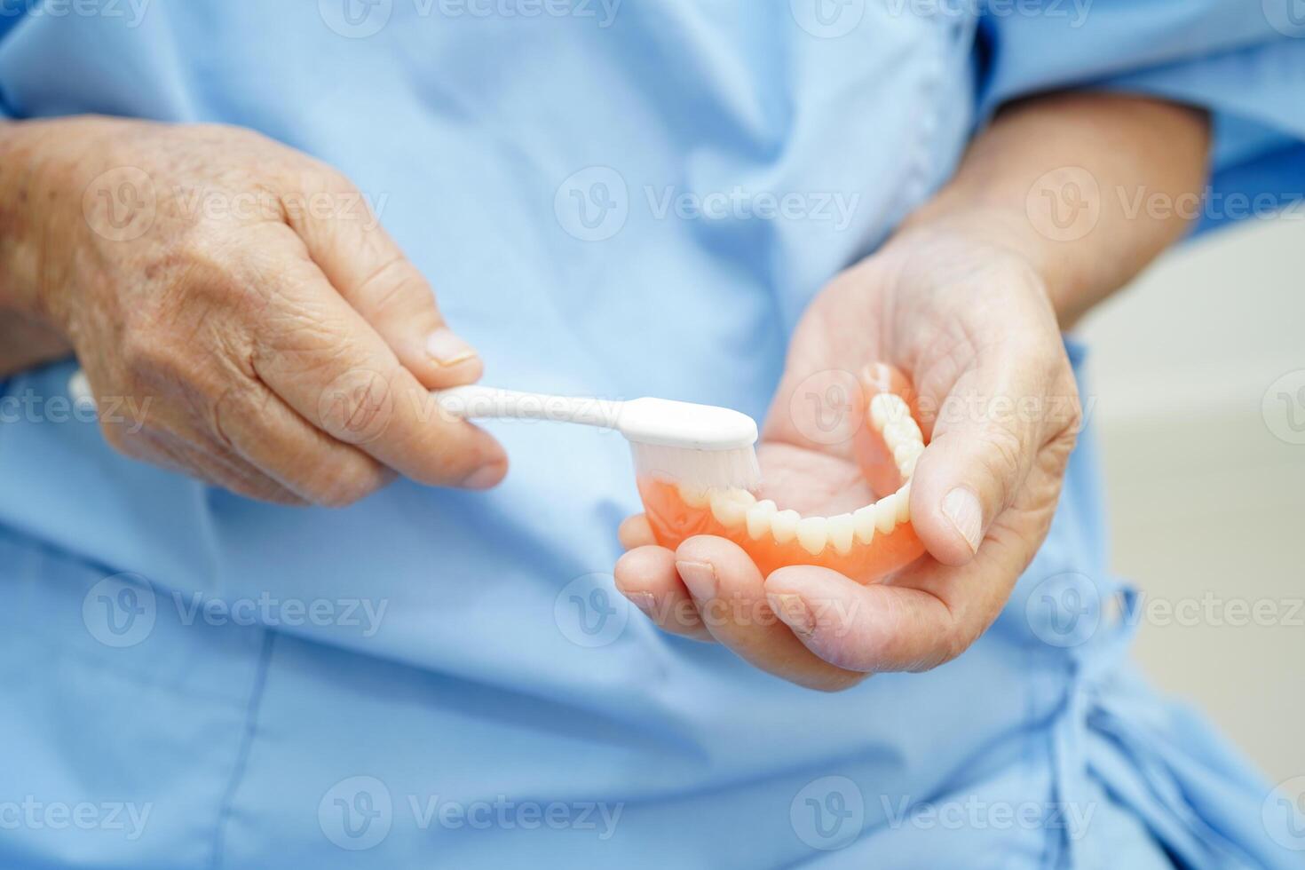 ásia Senior mulher paciente segurando dentes dentadura dentro dela mão para mastigar Comida. foto