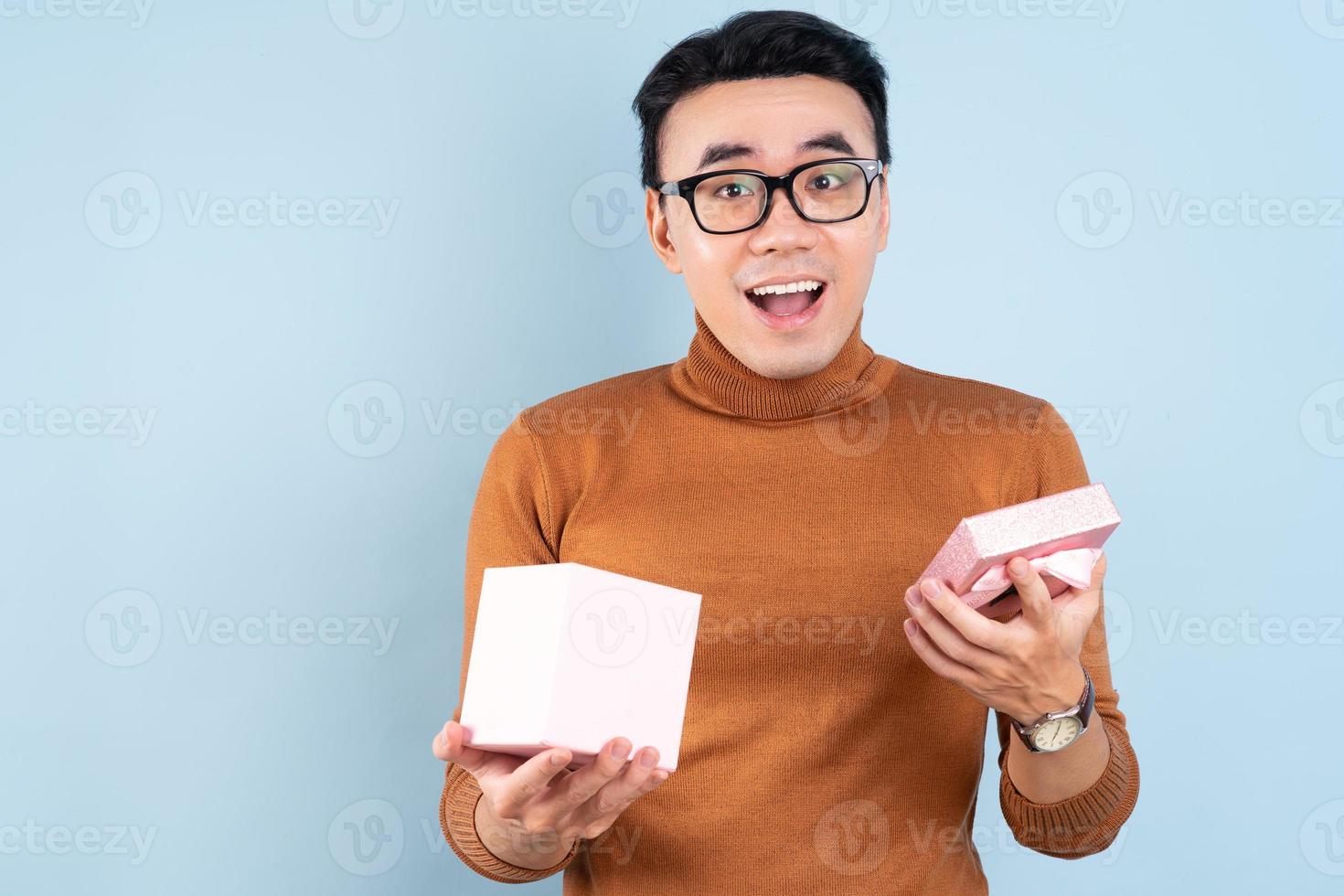 homem asiático segurando uma caixa de presente rosa sobre fundo azul foto