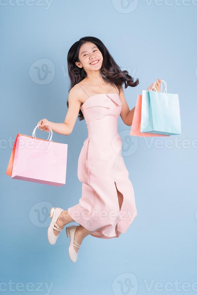 bela jovem asiática segurando uma sacola de compras sobre fundo azul foto