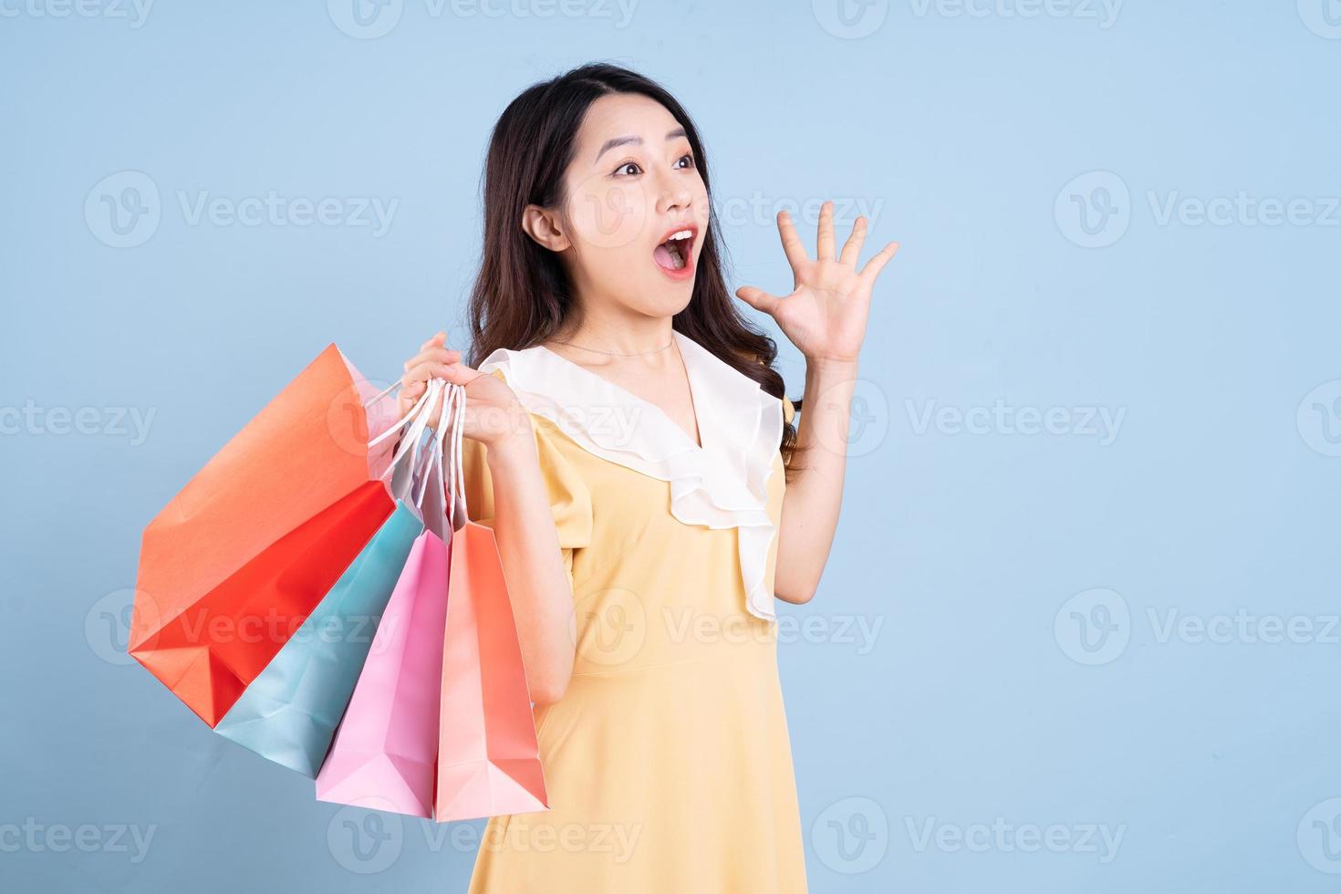 bela jovem asiática segurando uma sacola de compras sobre fundo azul foto