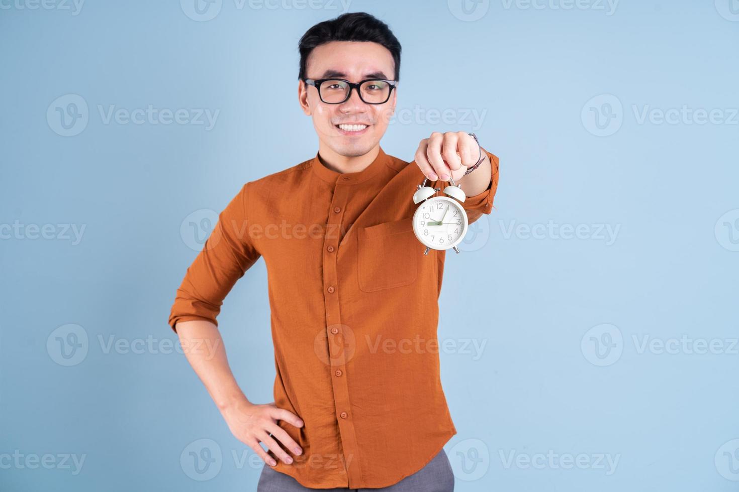 jovem asiático segurando o relógio no fundo azul foto