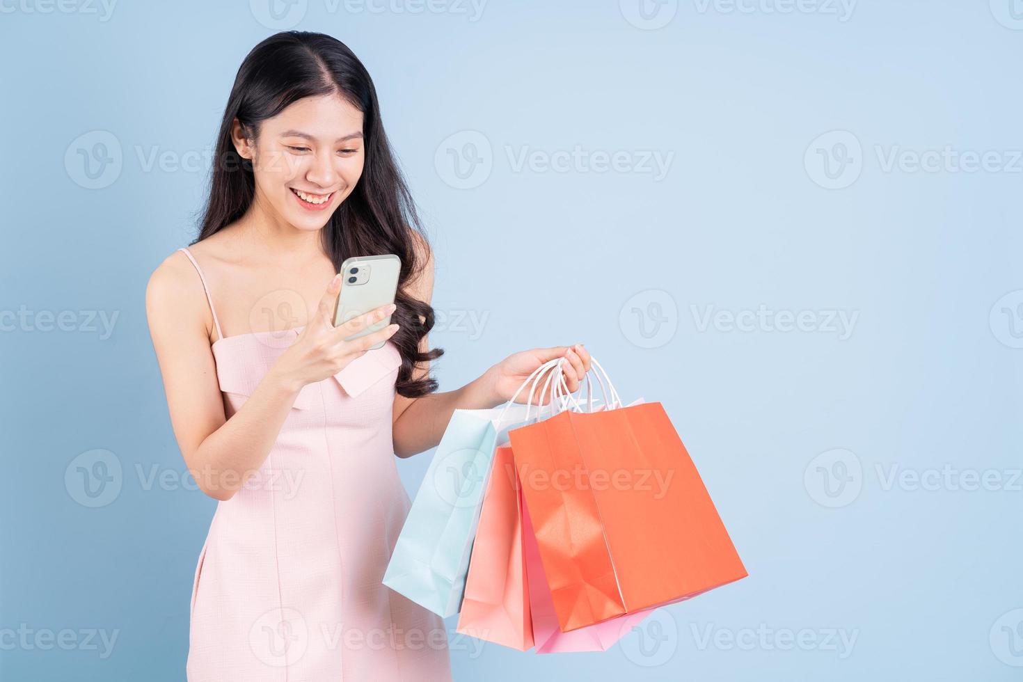 bela jovem asiática segurando uma sacola de compras sobre fundo azul foto