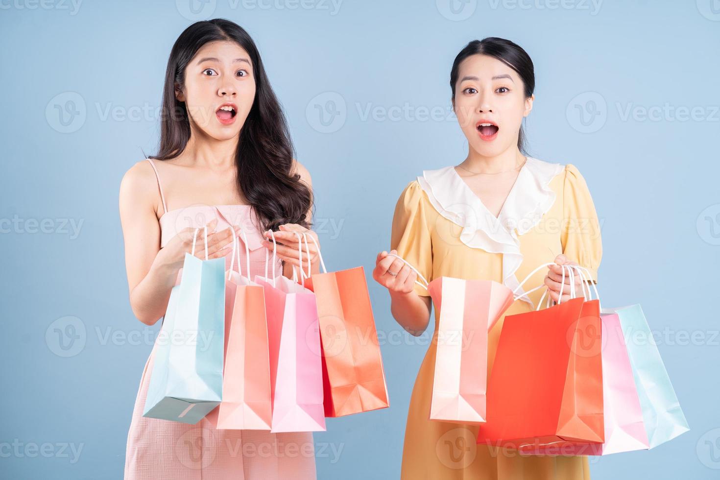 duas jovens mulheres asiáticas segurando uma sacola de compras sobre fundo azul foto