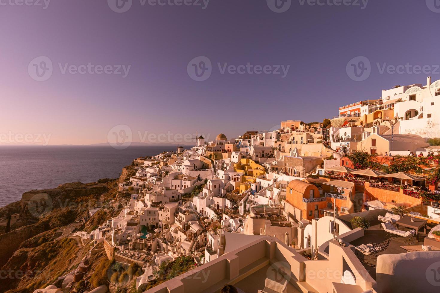 linda ilha do pôr do sol de santorini, grécia, bela vila caiada de branco oia com moinho de vento da igreja durante o pôr do sol, luzes das ruas, férias românticas de verão, destino de viagem de casal famoso em lua de mel foto