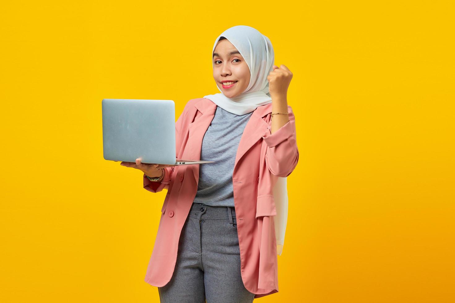 retrato de uma mulher asiática alegre segurando laptop e comemorando o sucesso isolado sobre fundo amarelo foto