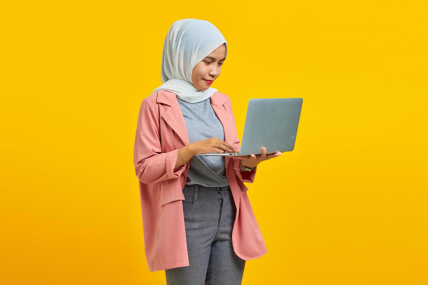retrato de uma bela jovem estudante universitária com laptop sorrindo vestindo uma jaqueta rosa isolada no fundo azul foto