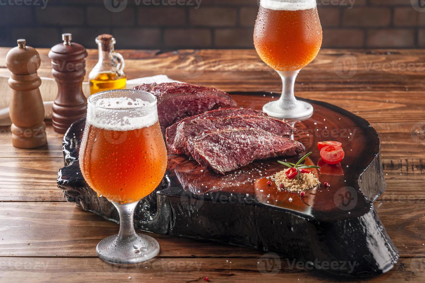 bife de denver grelhado na tábua de madeira com dois copos de tulipa gelada e suada de cerveja ale. carne bovina em mármore. foto