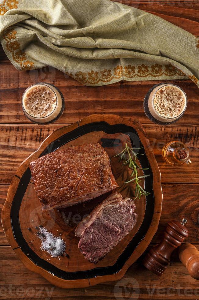 Lombo de tira grelhado na tábua de madeira com dois copos de chope escuro - vista superior. foto