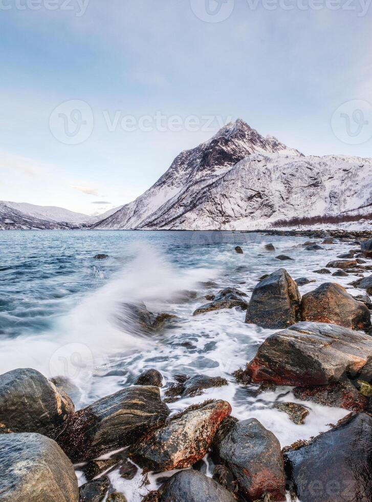 onda marinha batendo rochas com montanhas na costa ártica foto