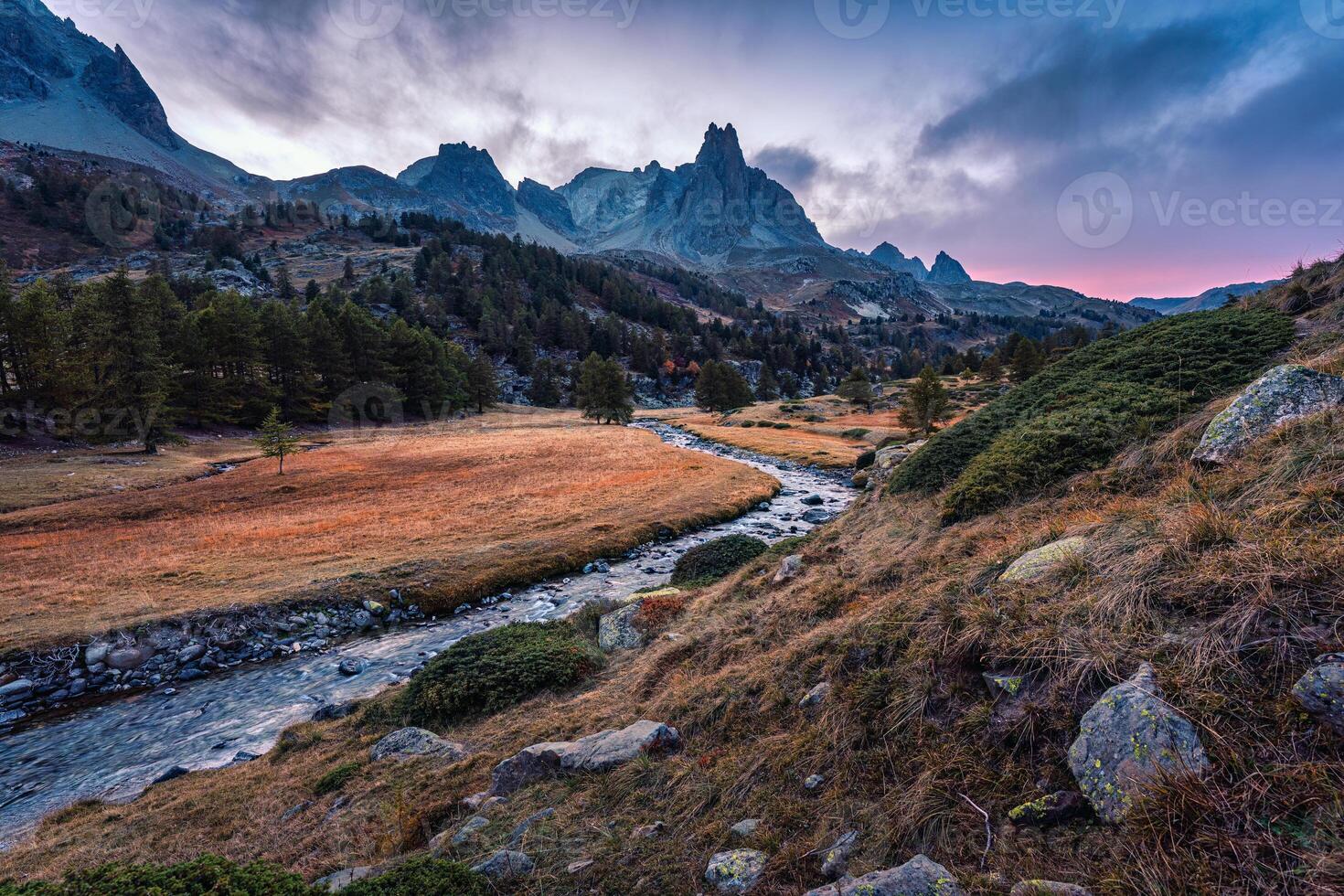 pôr do sol sobre Clare vale com a Principal de crepino pico e rio fluxo através dentro lariço floresta durante outono às francês Alpes, França foto