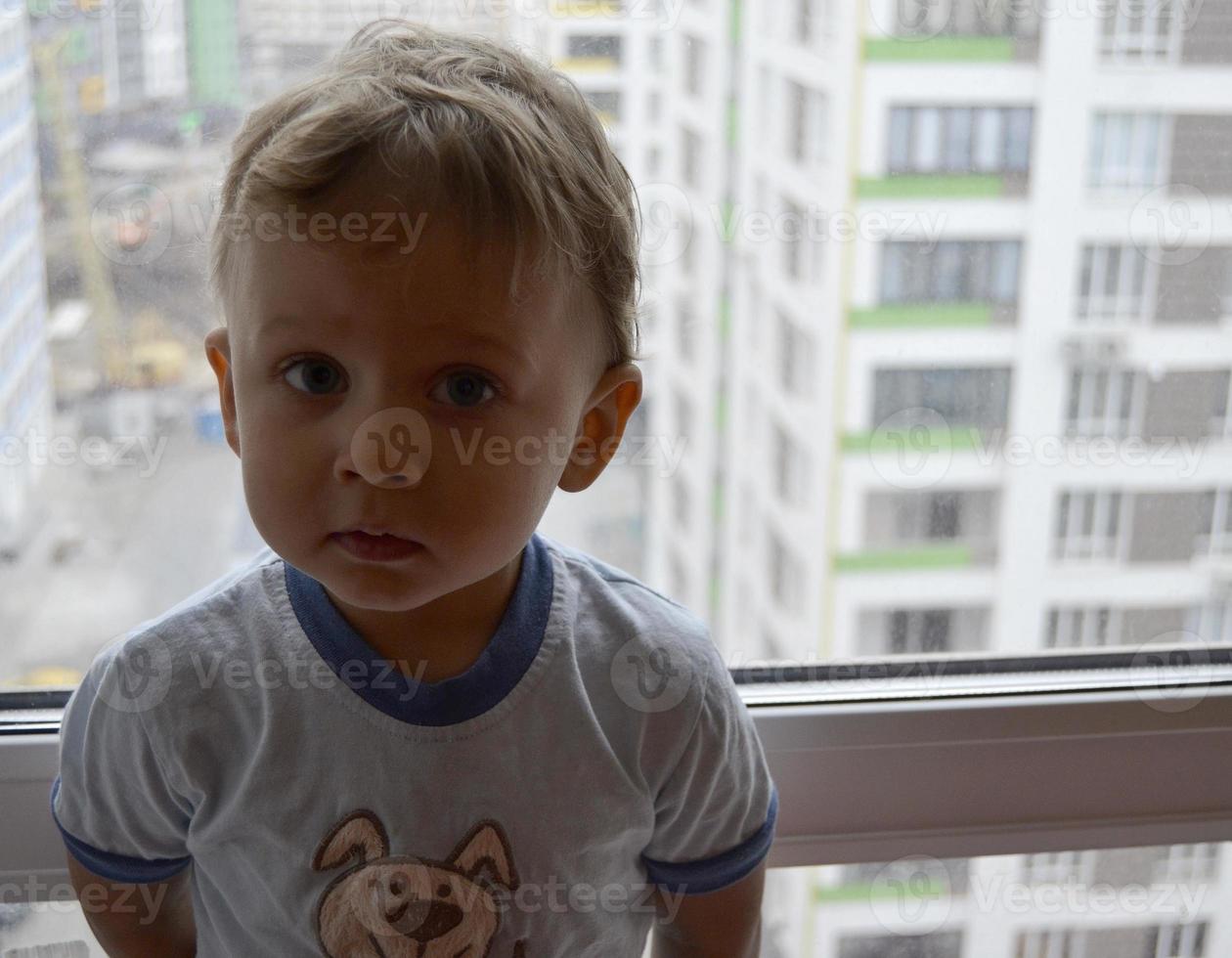 lindo menino com rosto de criança posando para fotógrafo perto da janela foto