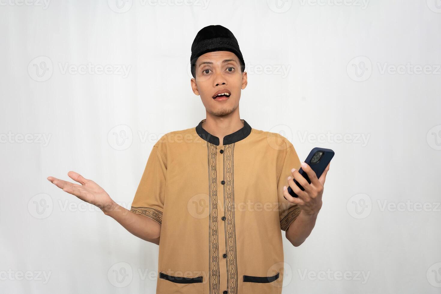 ásia muçulmano homem vestindo muçulmano roupas é chocado, confuso e surpreso enquanto carregando uma Smartphone. isolado branco fundo. foto