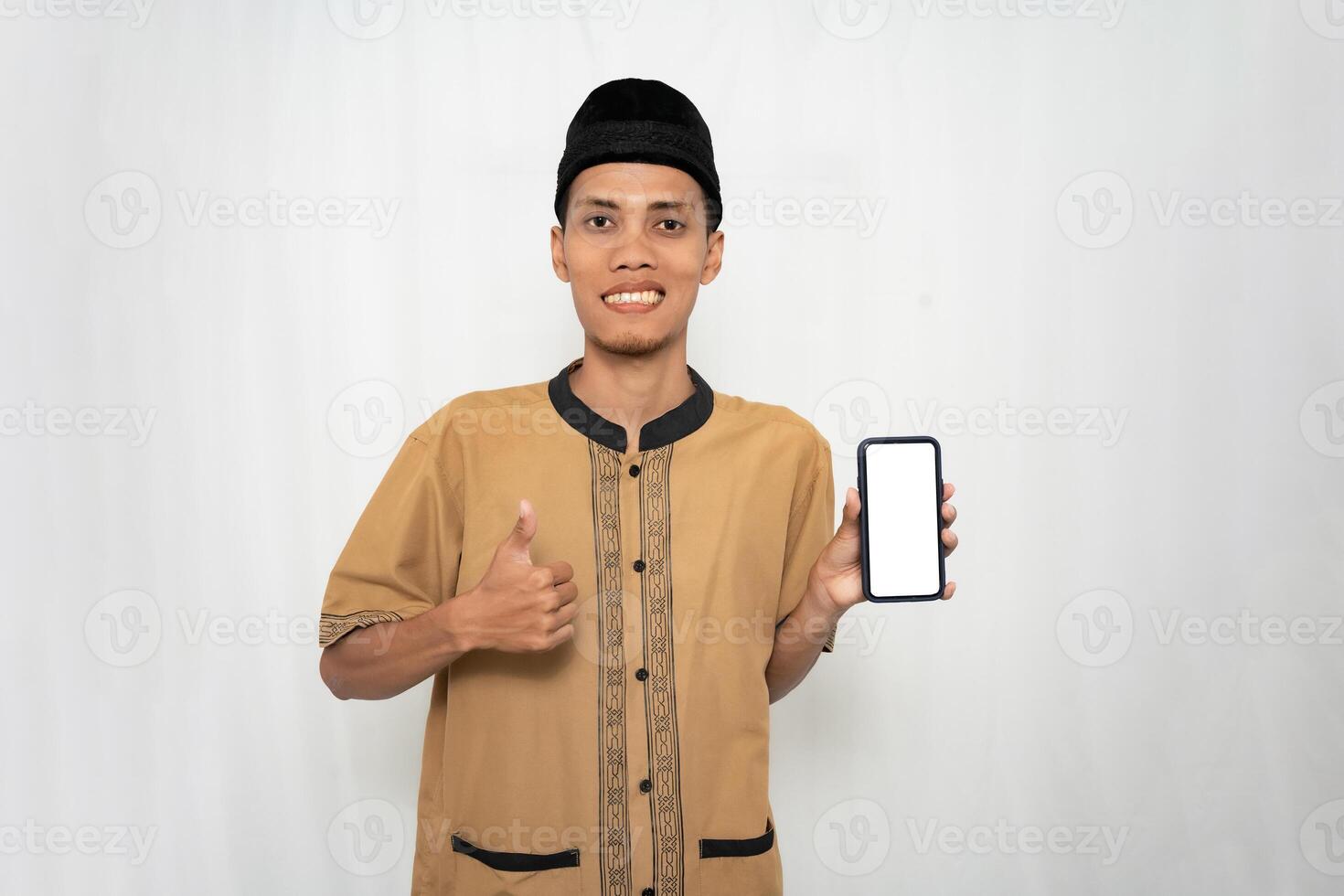 ásia muçulmano homem vestindo Castanho muçulmano roupas sorridente alegremente enquanto apontando às a Smartphone tela. isolado branco fundo. foto