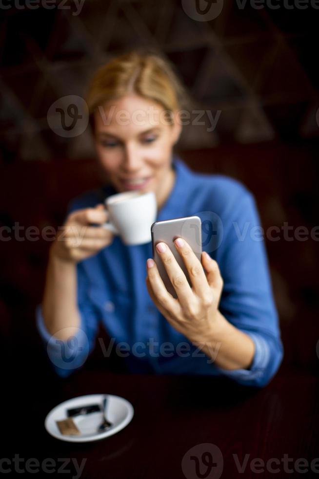 bela jovem sentada à mesa com café ou cappuccino e usando o telefone celular foto