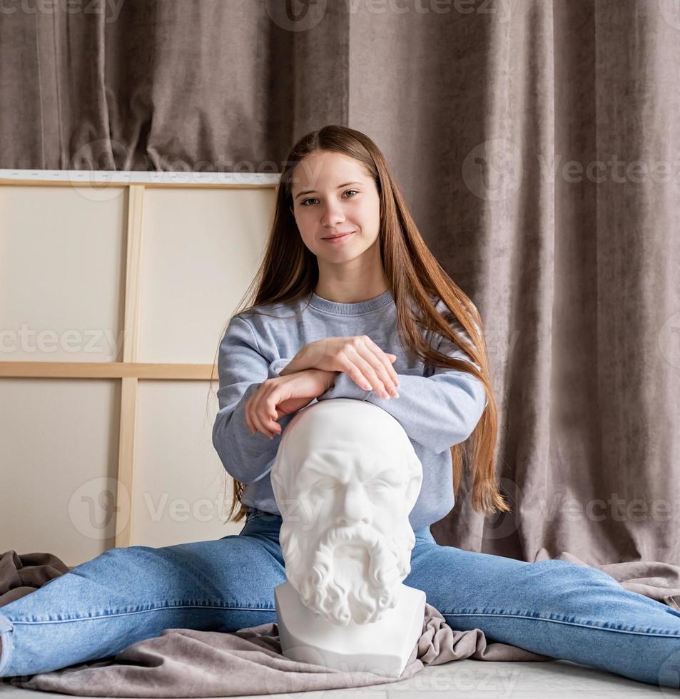 jovem artista sentada em seu estúdio com a tela e a cabeça de socrates de gesso foto