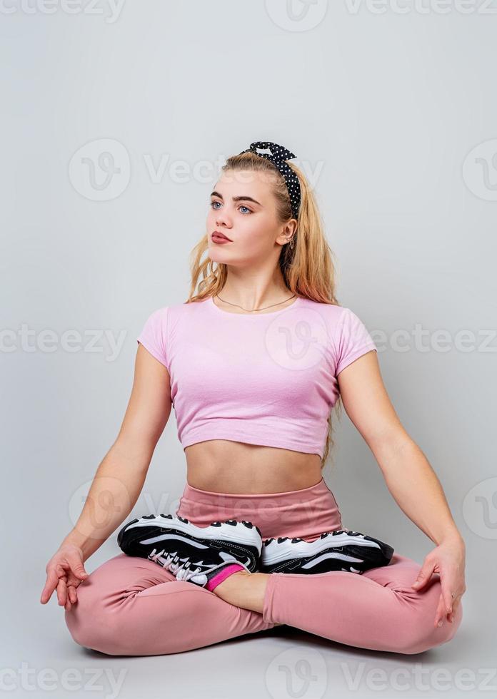 bela jovem caucasiana sentada em posição de ioga e meditando isolada sobre um fundo cinza foto