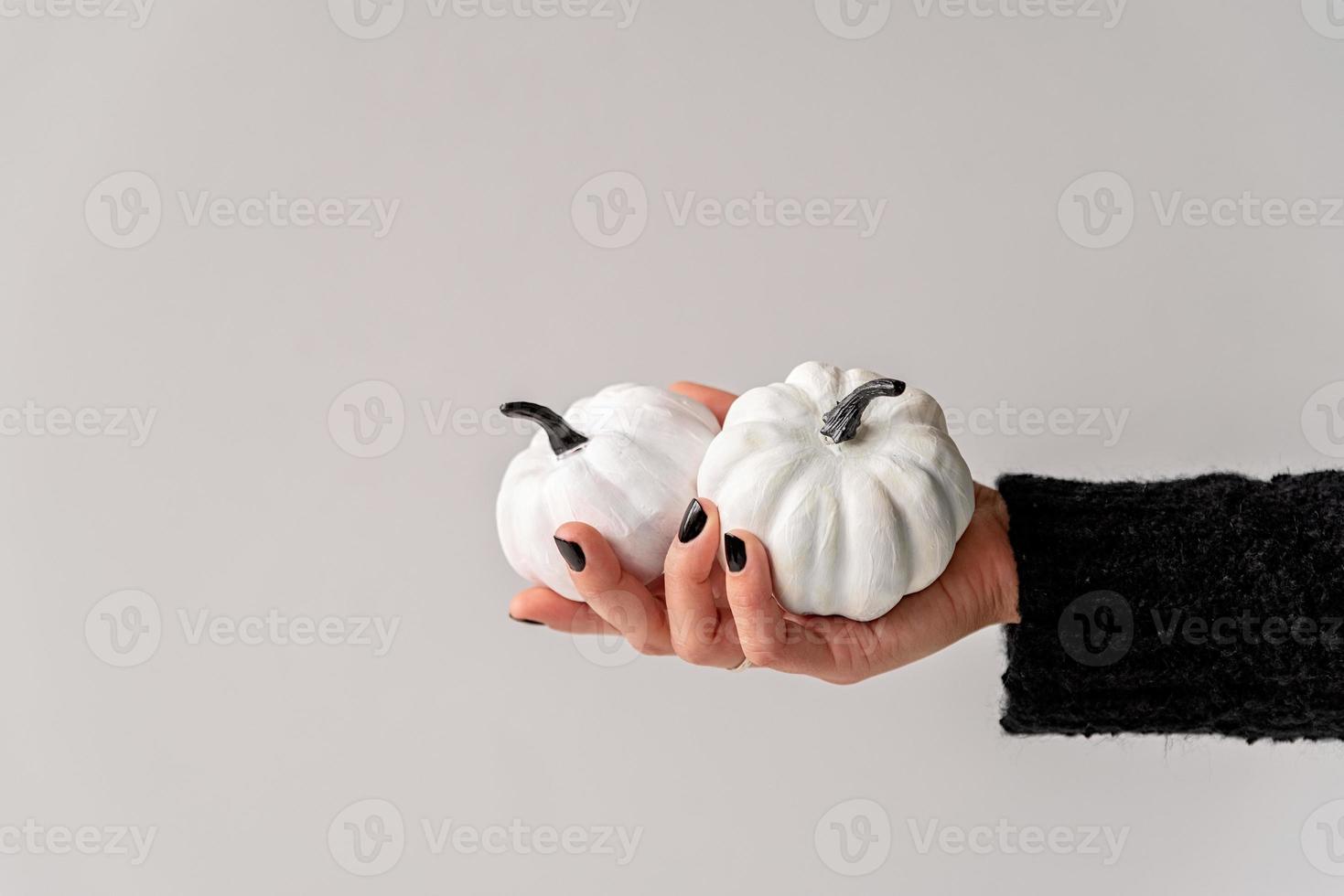 mão feminina com unhas pretas segurando abóboras de halloween brancas e pretas foto