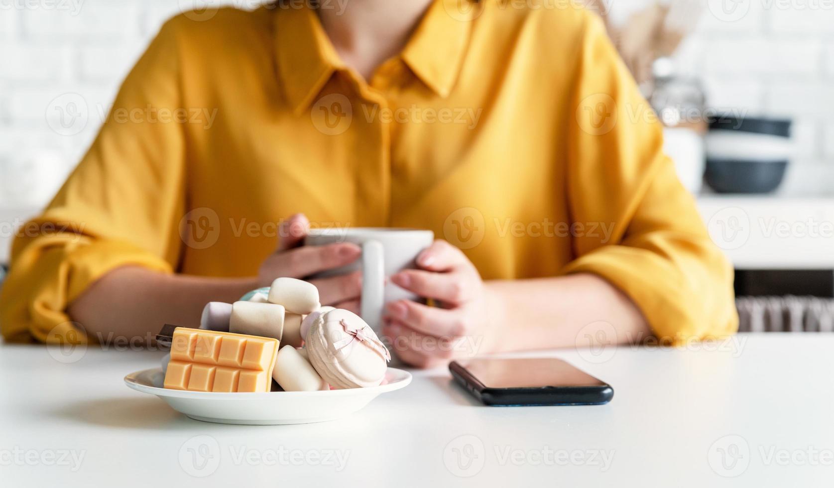 mulher comendo doces e tomando café na cozinha foto