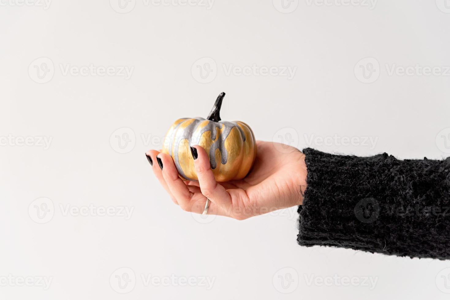 mão feminina com unhas pretas segurando uma abóbora de halloween ouro e preta foto