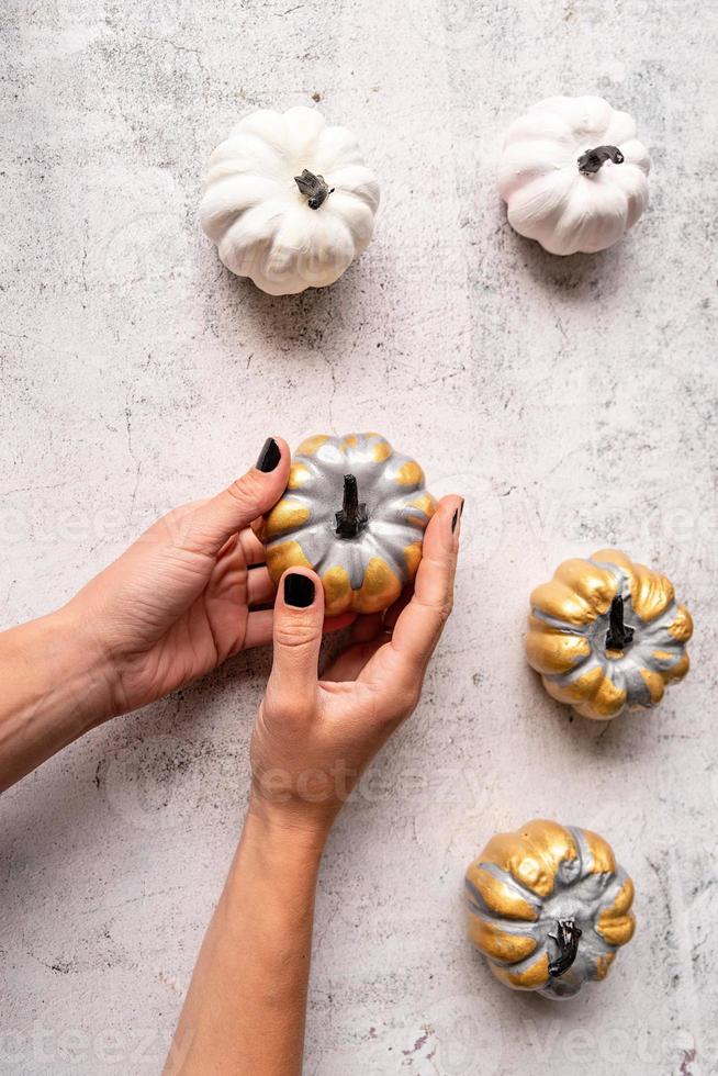 mãos de mulher com unhas pretas segurando uma abóbora dourada colorida foto