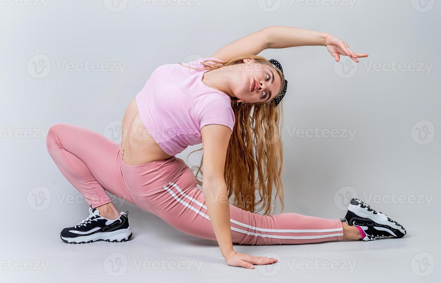 mulher acrobata vestindo roupas esportivas rosa alongamento no estúdio isolado em fundo cinza foto