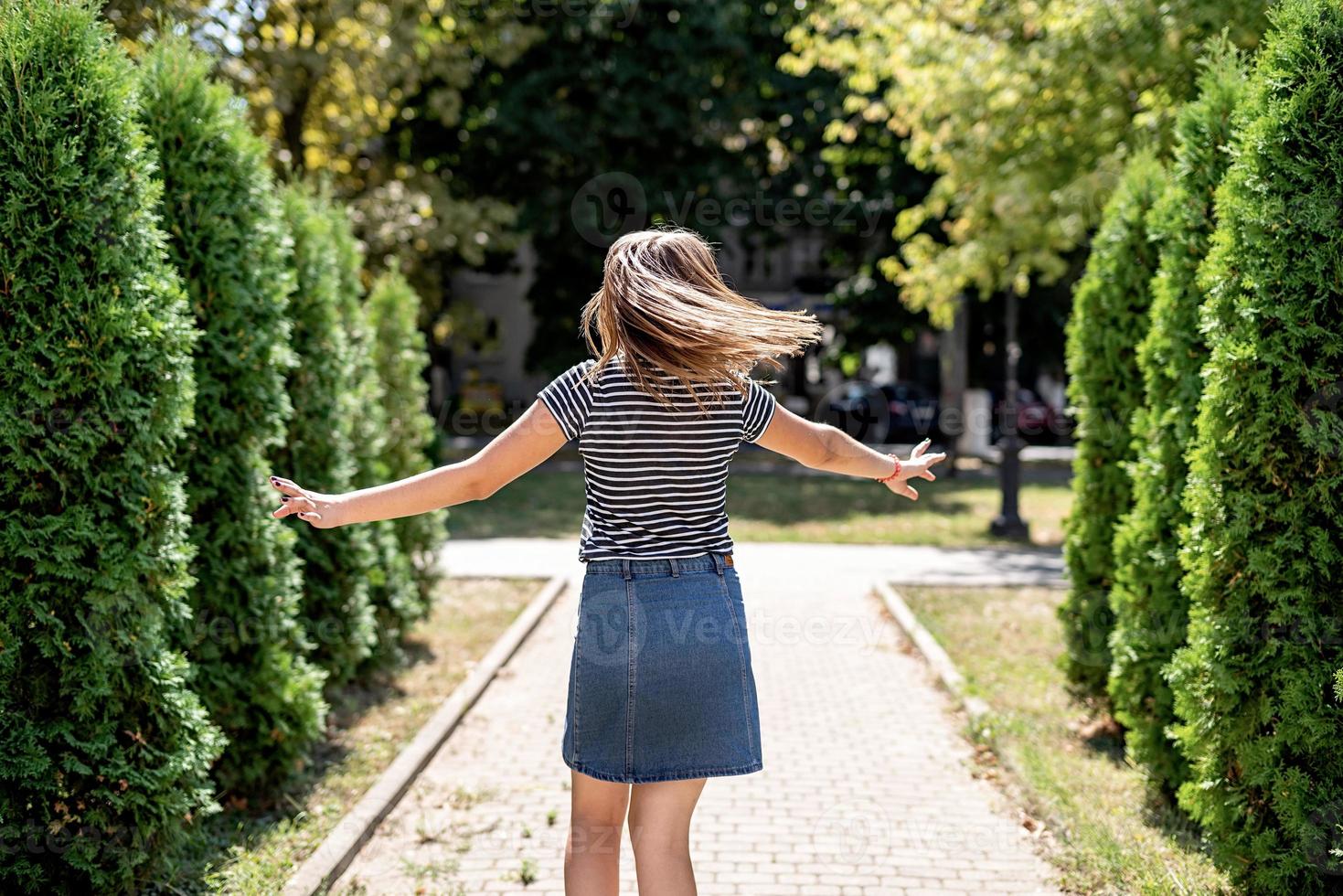 jovem mulher bonita caucasiana em roupas casuais se divertindo dando voltas no fundo das árvores no parque foto