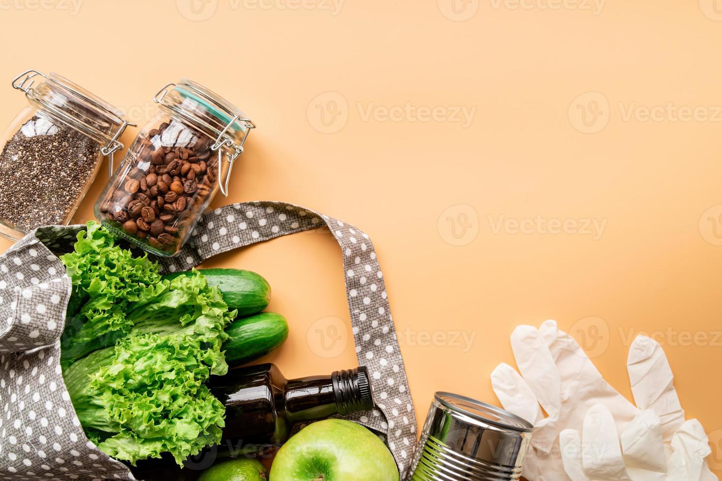 Saco ecológico com vegetais verdes, sementes de chia, luvas e vista superior de azeite em fundo laranja com espaço de cópia foto