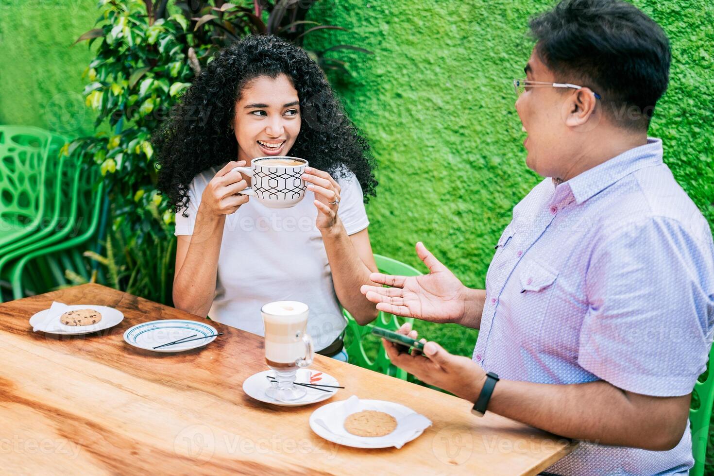 sorridente amigos falando e desfrutando café às uma mesa. conceito do amigos desfrutando uma Boa café. dois feliz amigos tendo uma café e falando foto