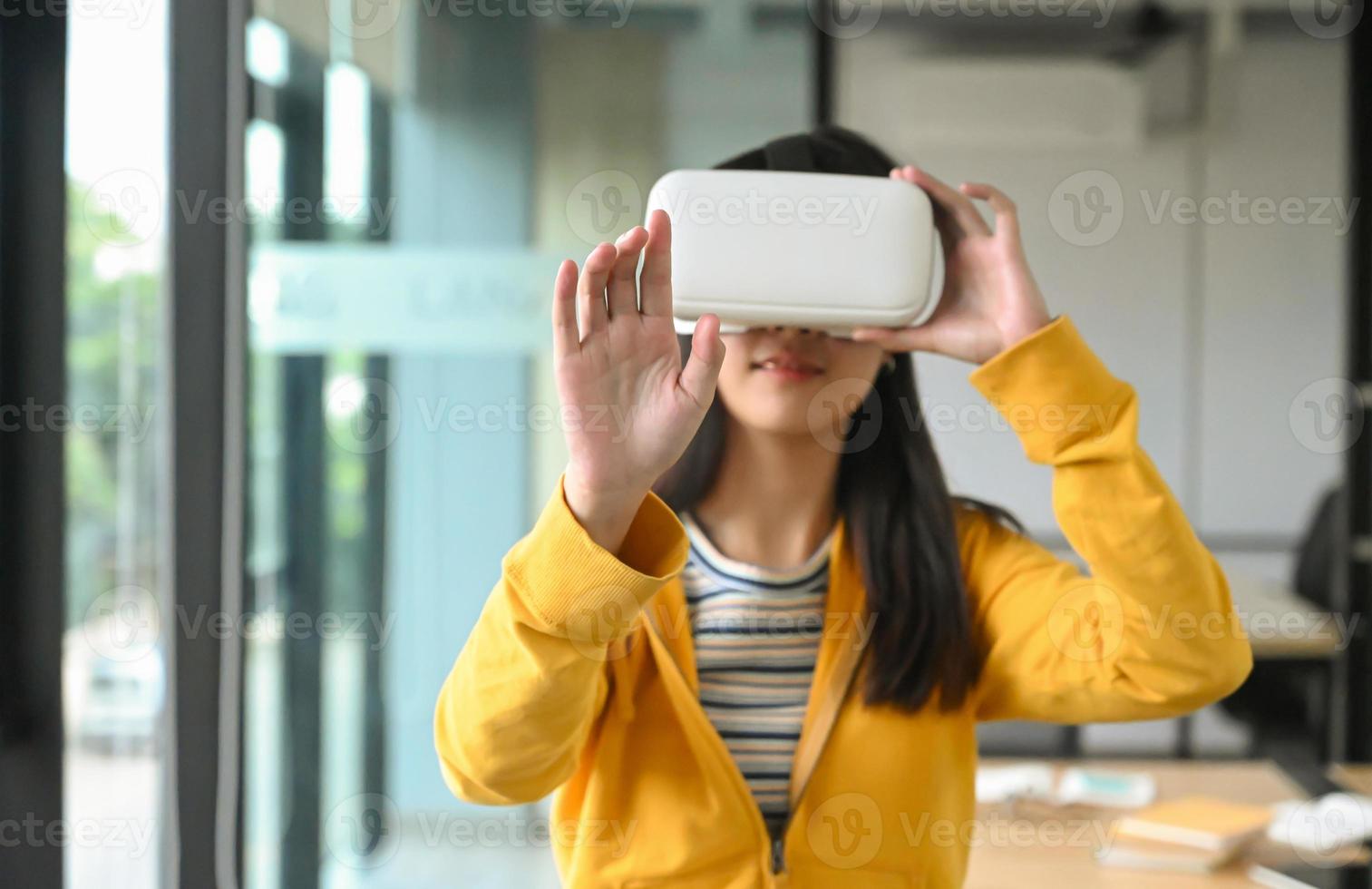 menina asiática está vestindo uma camisa amarela usando fone de ouvido vr. Ela apontou a mão na frente e estava sorrindo. foto