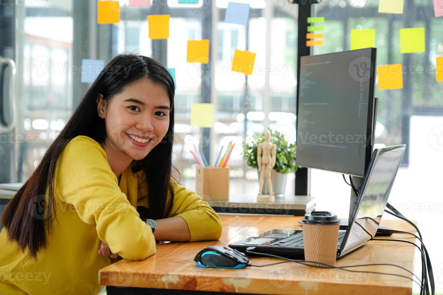programadora asiática de camisa amarela, sentada à sua mesa no escritório. ela olhou e sorriu feliz. foto