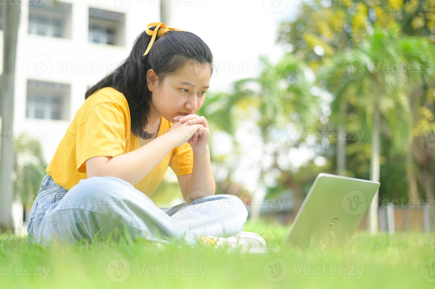 adolescente sentada no gramado, olhando para o laptop, trabalhar em casa. foto