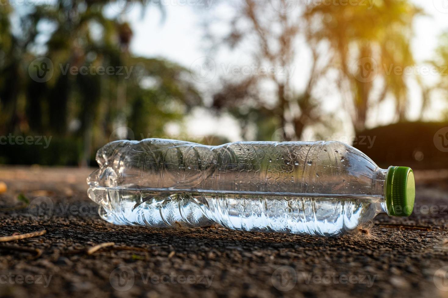 feche uma garrafa de plástico transparente bebida de água com uma tampa verde na estrada no parque no fundo desfocado, lixo que é deixado do lado de fora da lixeira foto