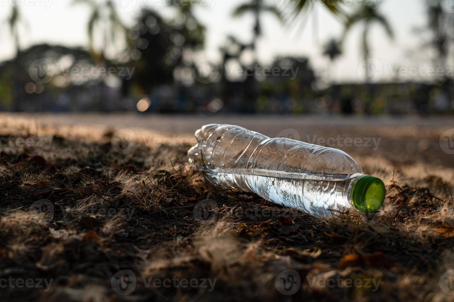feche uma garrafa de plástico transparente bebida de água com uma tampa verde na estrada no parque no fundo desfocado, lixo que é deixado do lado de fora da lixeira foto