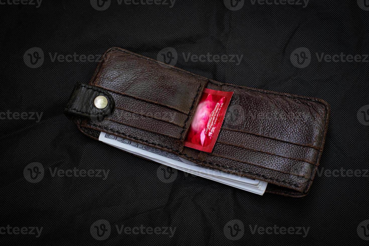 carteira de couro preto closeup com um preservativo vermelho no fundo preto foto