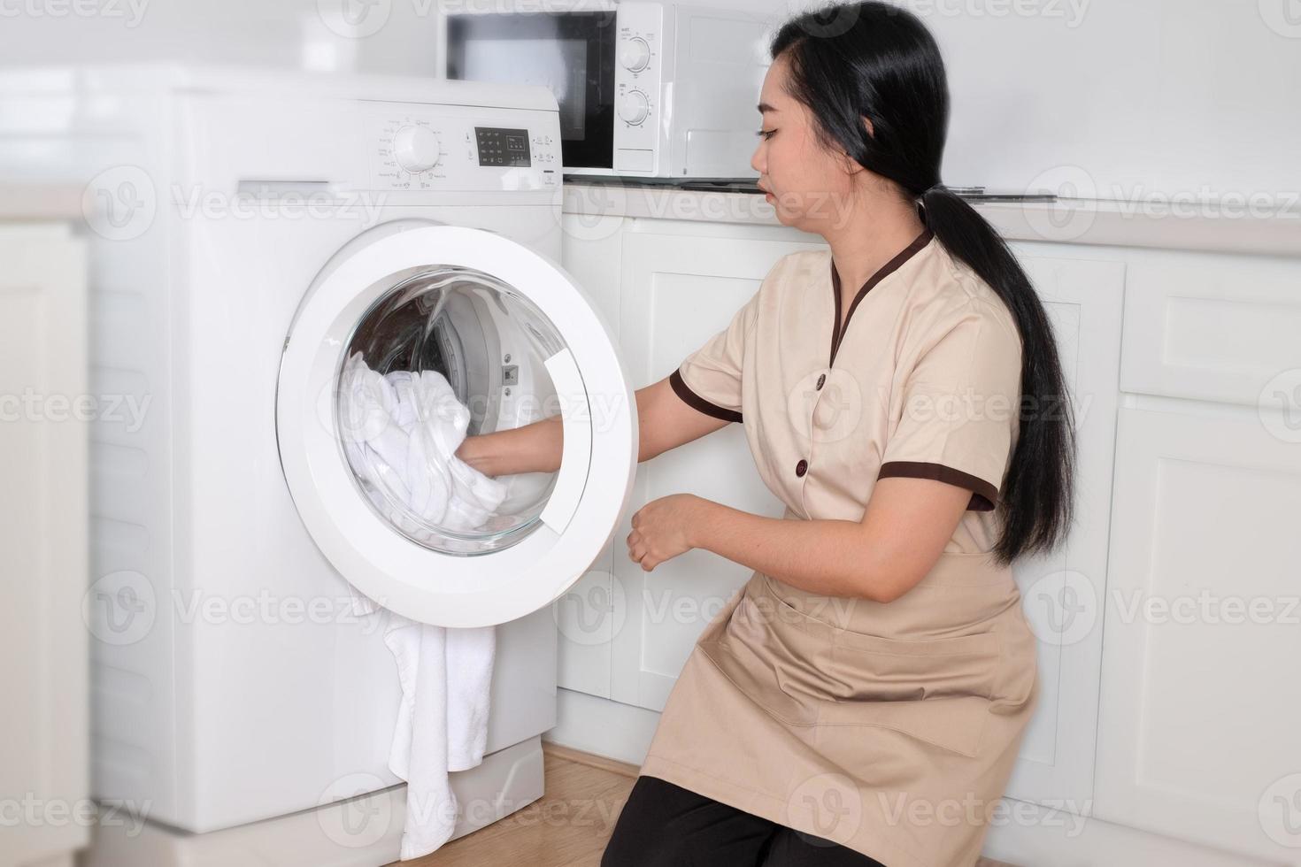 jovem bela empregada asiática carregando a máquina de lavar roupas brancas no quarto do hotel foto