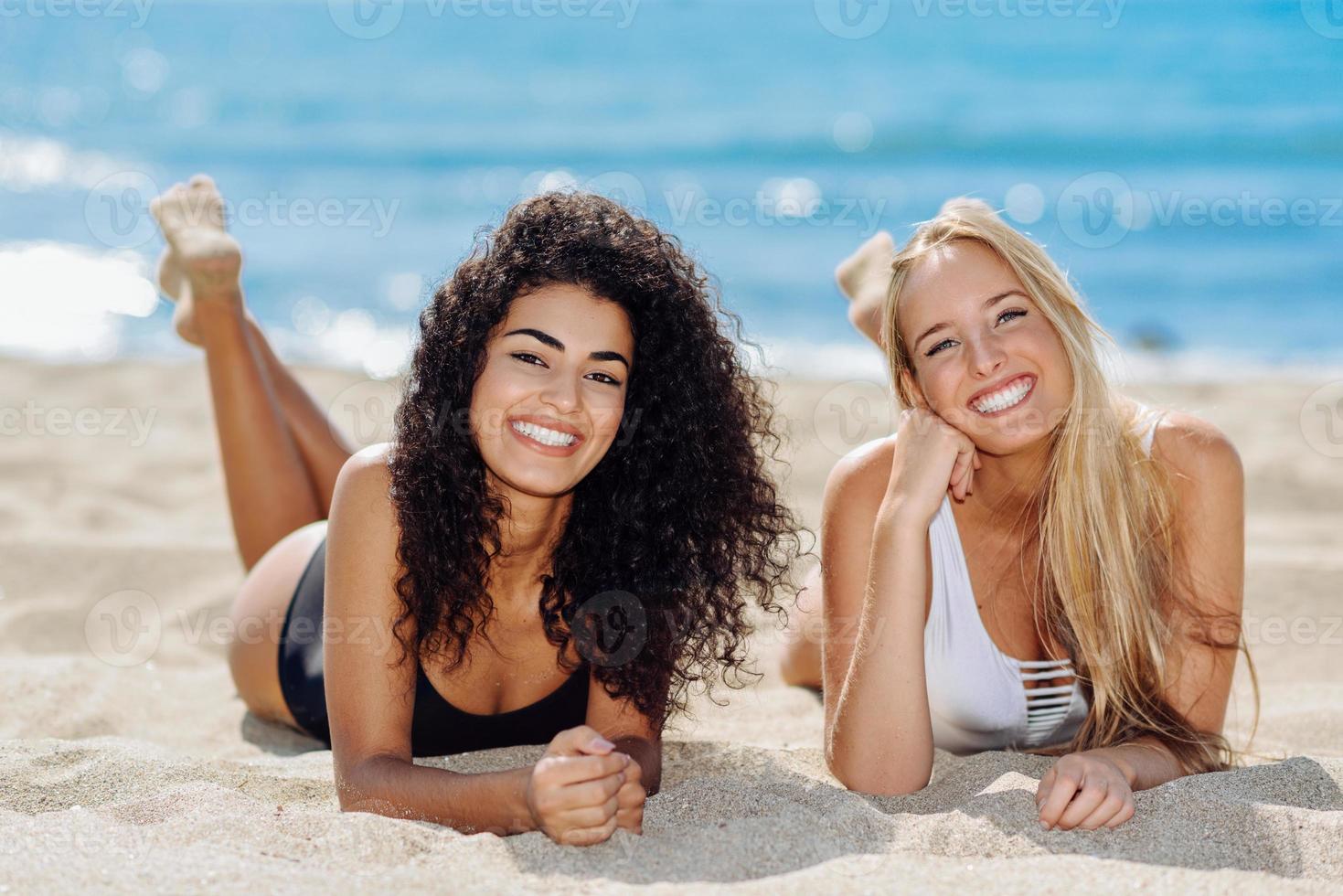 duas mulheres jovens com belos corpos em maiô em uma praia tropical foto