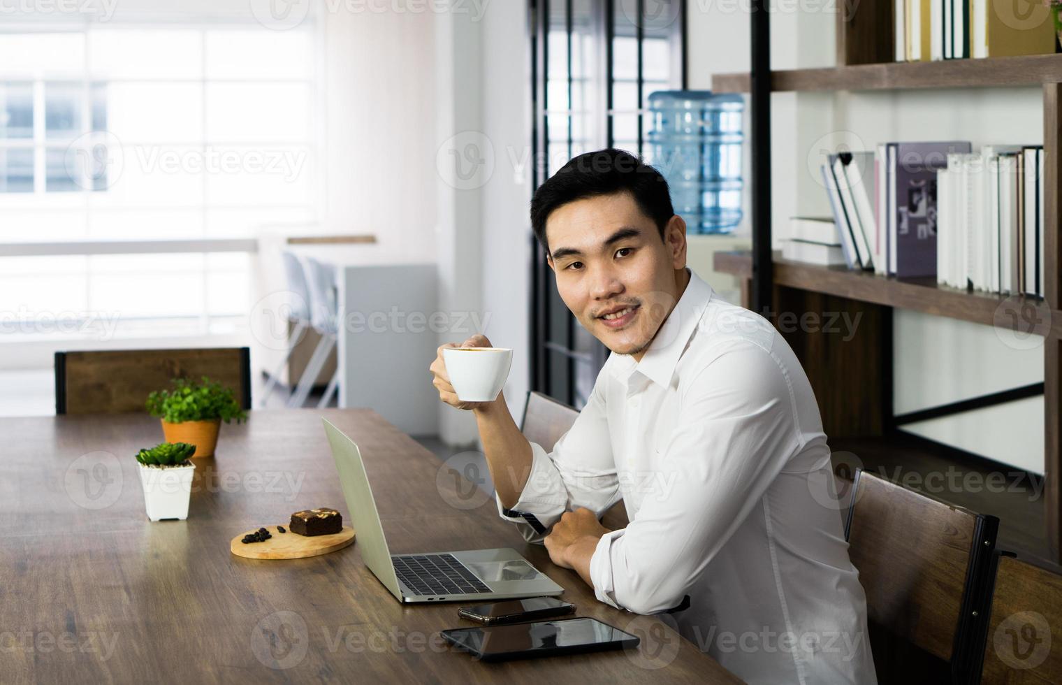 homem asiático sentado no café, bebendo café e café da manhã, woking a distância. conceito de negócios e tecnologia foto
