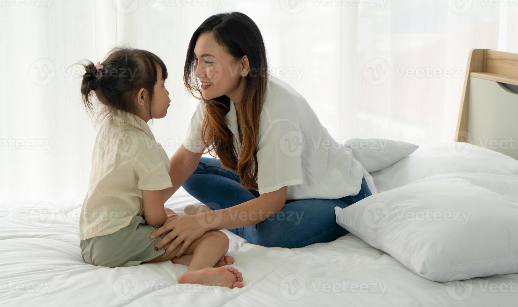 mãe asiática e criança com um rosto sorridente sentados juntos na cama no quarto foto