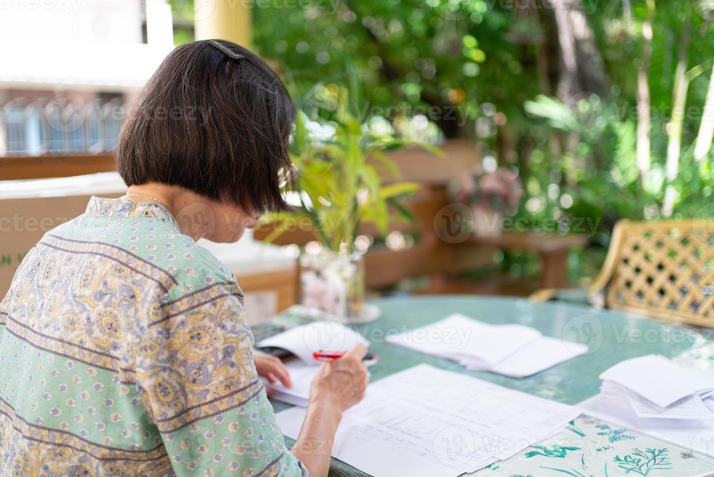 mulher asiática sênior calcula o saldo de receitas e despesas no terraço de casa foto