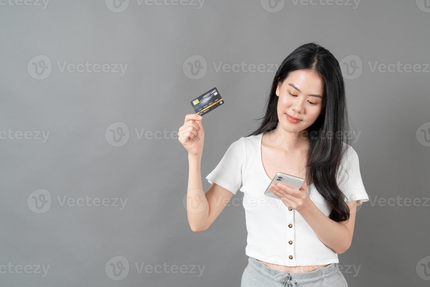 jovem mulher asiática usando telefone com a mão segurando um cartão de crédito foto