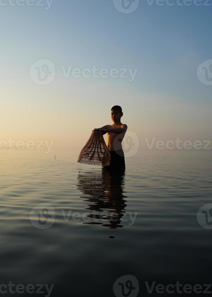 no lago, jovem asiático usando armadilha de bambu para pescar de manhã foto