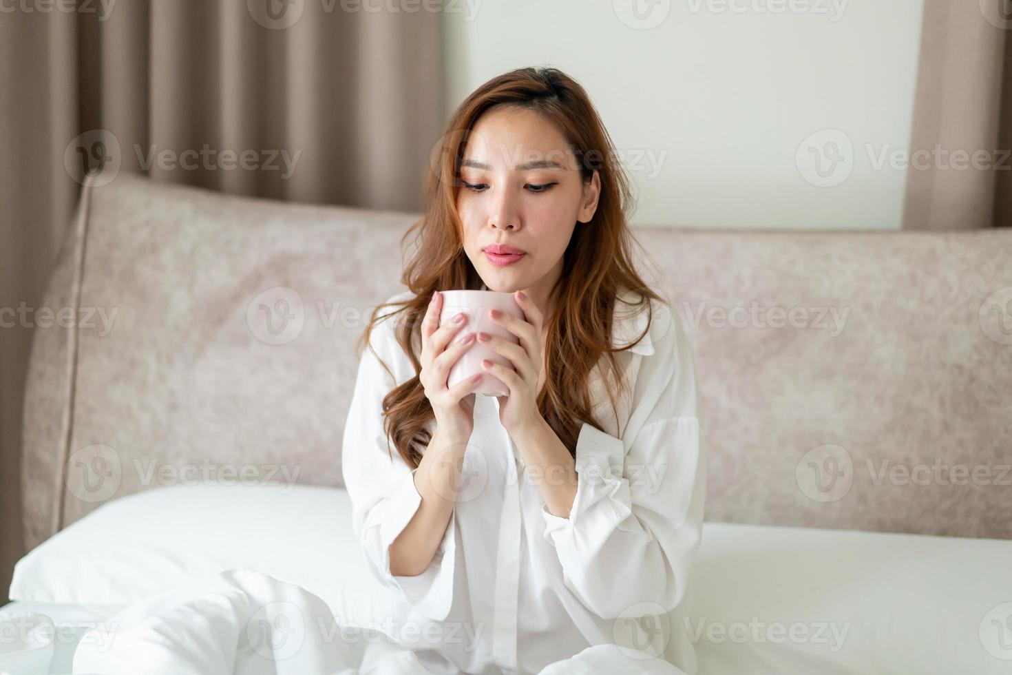 retrato de mulher bonita acordar e segurando uma xícara de café ou caneca na cama foto