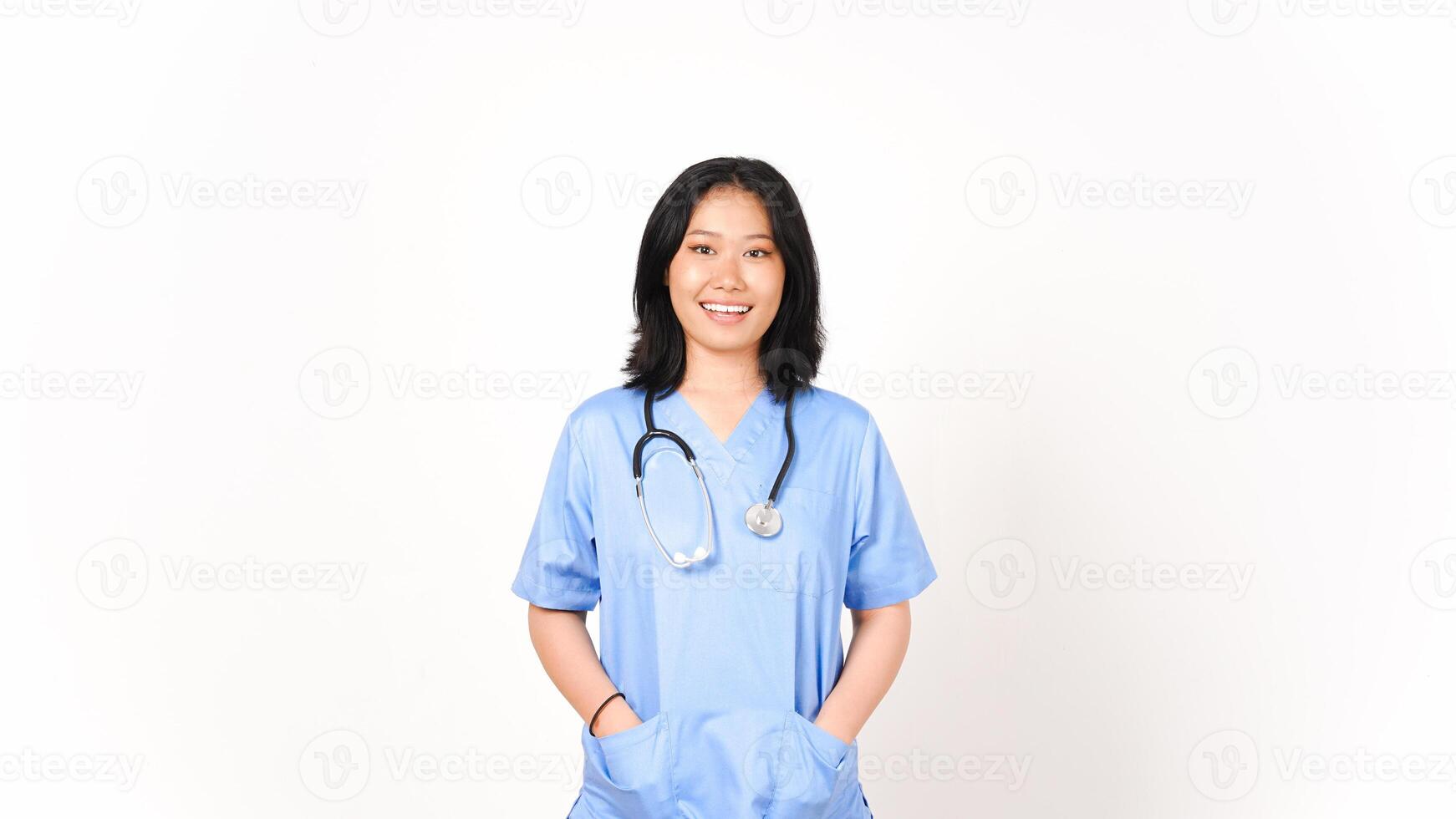 jovem ásia fêmea médico mãos em bolso olhando Câmera e sorrir isolado em branco fundo foto