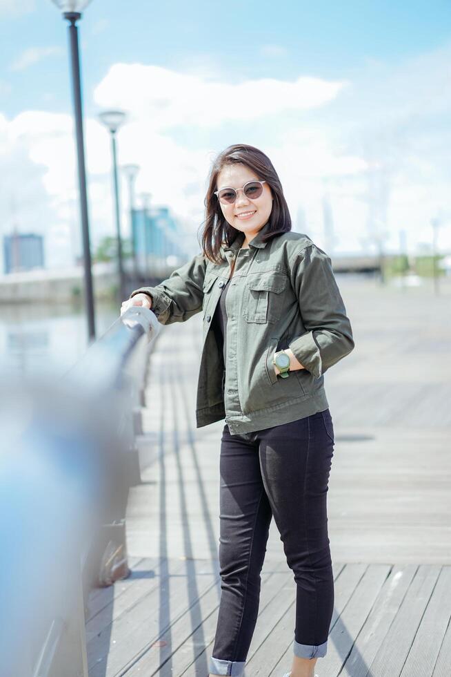 jovem lindo ásia mulher vestindo Jaqueta e Preto jeans posando ao ar livre foto