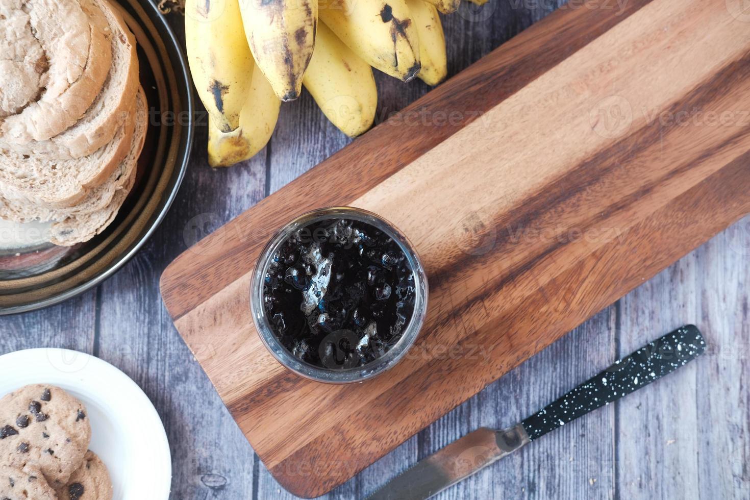 geléia de baga azul em um recipiente com pão e banana na mesa foto