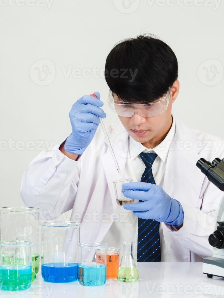 retrato ásia homem aluna cientista vestindo uma médico vestido dentro a laboratório olhando mão às químico. causou de mistura reagentes dentro científico pesquisa laboratórios com teste tubos e microscópio em a mesa foto