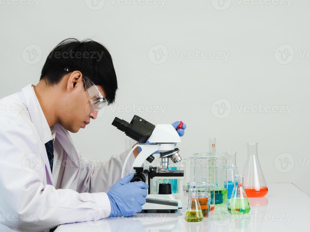 retrato ásia homem aluna cientista vestindo uma médico vestido dentro a laboratório olhando mão às químico. causou de mistura reagentes dentro científico pesquisa laboratórios com teste tubos e microscópio em a mesa foto